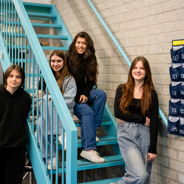Foto van vier meiden bij een trap zitten en staan